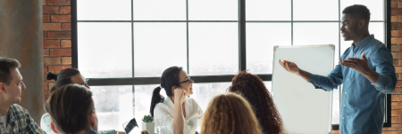 A man enthusiastically presents to a group of people during a corporate meeting.
