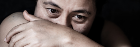 A person is seen in the dark, resting their head on their arm, with their hand wrapped around their arm.