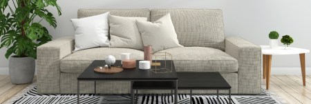 A couch with a coffee table in front of it and plants on both sides of it.