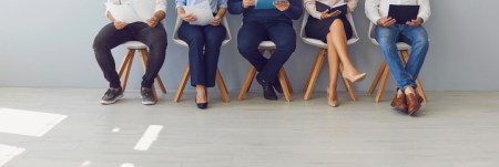 A group of job applicants sit in a row in a waiting area.