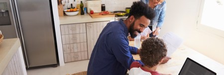 A family sits at the kitchen table. Mom and dad help the kids with homework.