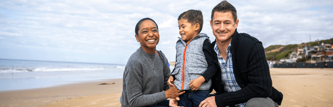A mother, father and their young child smile on the beach.