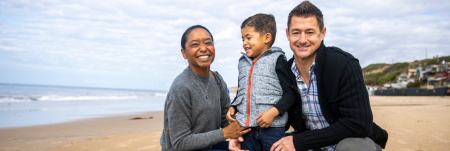 A mother, father and their young child smile on the beach.