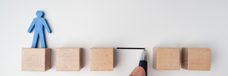 Five wooden blocks are lined up with a gap between them. A blue paper cutout of a person stands on the first wooden block.