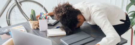 A woman rests her head on her desk in exhaustion.