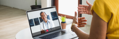 A doctor and their patient talk over a video call. The doctor is seen listening and smiling on screen.
