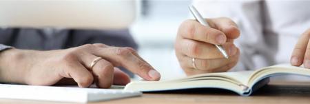 A close-up of two people's hands as they write in a notebook.