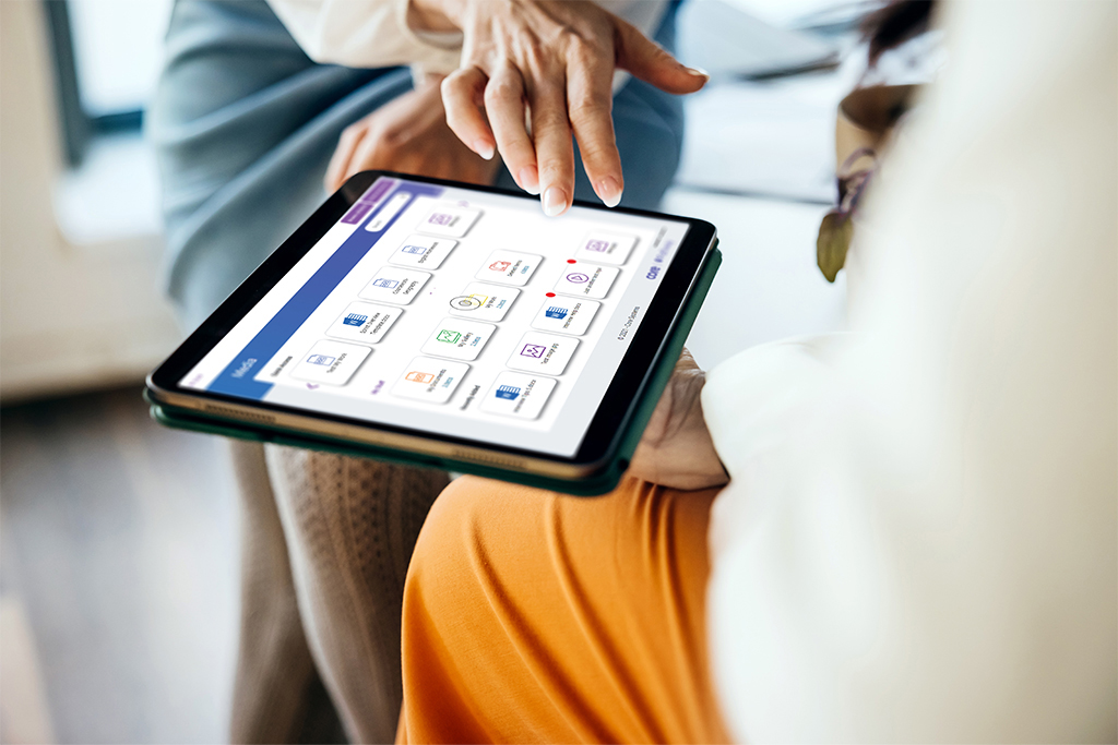 Close-up of two people interacting with a tablet device; one points at the screen displaying app icons while the other holds the tablet.