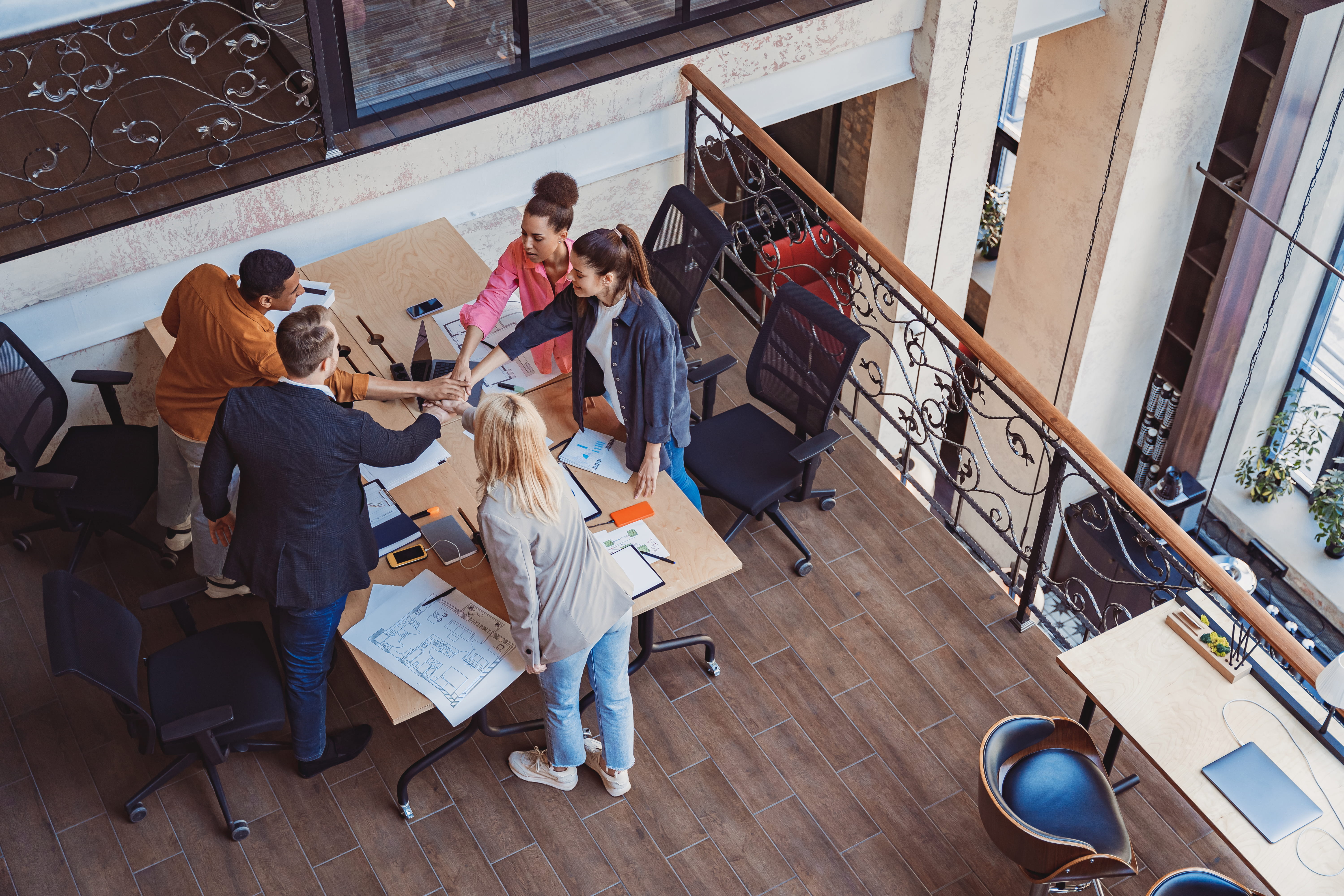 Team members gathered around a table stacking hands in a collaborative office. Team members gathered around a table stacking hands in a collaborative office.